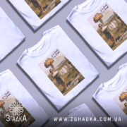 Футболка все під контролем. Білий колір, фронтальний ракурс, фон нейтральний. Принт з жінкою, яка тримає кошик з білизною на фоні вибуху, текст 'It's Fine, I'm Fine' та 'Everything's Fine'.