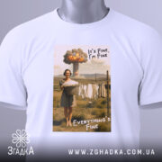 Футболка все під контролем. Білий колір, ракурс зверху, фон світлий. Принт з жінкою, яка тримає кошик з білизною, текст 'It's Fine, I'm Fine' та 'Everything's Fine', на ярлику зелена стрічка.