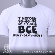 Футболка все сексі вайб, складена біла футболка з чорним принтом, зображена зверху, фон світлий, на футболці є етикетка з зеленим шнурком, принт містить текст з жартом про розміри.