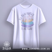 Футболка все що не робиться, білого кольору, підвішена на вішалці, фон світло-сірий. Принт з котом на кольорових паперах, текст українською мовою.