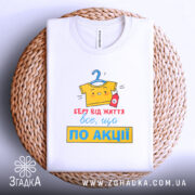 Футболка все, що по акції. Біла футболка, складена на плетеній основі, фон світлий. Принт яскравий, з жовтою футболкою на вішалці та червоною пляшечкою, текст червоний і жовтий.