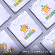 Футболка все, що по акції. Біла футболка з коротким рукавом, зображена з правого ракурсу на манекені. Фон світло-сірий, принт на футболці яскравий, з жовтою футболкою, що висить на вішалці, та червоним пляшечкою, текст червоний і жовтий.