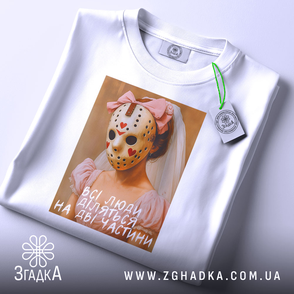 Футболка всі люди діляться, біла, зображена з верхнього ракурсу, на фоні світло-сірого градієнта, принт з дівчиною в рожевій сукні та масці, з червоними сердечками, підпис на принті: 'всі люди діляться на дві частини', з етикеткою на рукаві.