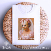 Футболка всі люди діляться, біла, зображена з верхнього ракурсу, на фоні плетеного кошика, принт з дівчиною в рожевій сукні та масці, з червоними сердечками, підпис на принті: 'всі люди діляться на дві частини'.