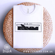 Футболка ви ще тут, білого кольору, складена на плетеній кошику, фон світло-сірий, принт чорного кольору з зображенням кота, який виглядає з коробки, текст "ВИ ЩЕ ТУТ?".