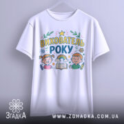 Футболка вихователь року, біла, підвішена на вішалці, принт яскравий, зображує дітей, книжку та інші елементи, фон однотонний.