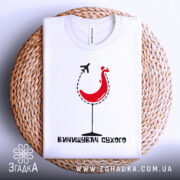 Футболка винищувач сухого білого кольору, зображена зверху на плетеній основі, фон світлий, принт з червоним курчам у келиху та літаком, текст під принтом чорного кольору.