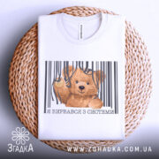 Футболка вирвався з системи, біла, складена на плетеному кошику, фон світло-сірий, принт з ведмедиком, що виглядає з-під смужок, текст під принтом українською мовою.