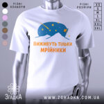 Футболка виживуть тільки мрійники. Біла футболка з принтом, на якому зображено синій малюнок, що нагадує космічну істоту, оточену зірками. Текст на футболці виконаний оранжевим кольором. Фон нейтральний, з легким градієнтом.