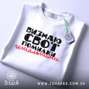 Футболка визнаю свої помилки, білого кольору, складена на плоскій поверхні, фон світло-сірий, принт чорного кольору з червоним акцентом, текст розташований по центру, на комірці видна етикетка.