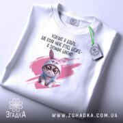 Футболка взагалі я добра. Білий колір, зображена в горизонтальному положенні, фон світло-сірий. Принт з кішкою в зайцевому капюшоні та текстом на українській мові, з зеленим ярликом.