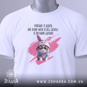 Футболка взагалі я добра. Білий колір, зображена в горизонтальному положенні, фон світло-сірий. Принт з кішкою в зайцевому капюшоні та текстом на українській мові, з зеленим ярликом.