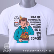 Футболка вже під 40, білого кольору, зображена зверху, на плоскій поверхні, фон світло-сірий, принт з ілюстрацією хлопця з тортом і текстом про вік, на футболці є етикетка.