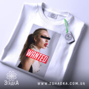 Футболка wanted стиль, біла, складена на поверхні, фон світло-сірий, принт з профільним зображенням жінки з червоними губами та написом 'WANTED' на червоному фоні, з етикеткою на комірці.