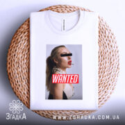 Футболка wanted стиль, біла, складена на плетеній основі, фон світло-сірий, принт з профільним зображенням жінки з червоними губами та написом 'WANTED' на червоному фоні.