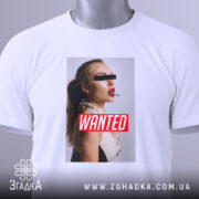 Футболка wanted стиль, біла, складена на поверхні, фон світло-сірий, принт з профільним зображенням жінки з червоними губами та написом 'WANTED' на червоному фоні, з етикеткою на комірці.