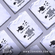 Футболка з філософією: біла футболка на манекені, з принтом чорного кольору, що містить зображення риб, текст "Don't panic, organize!". Фон світло-сірий, футболка має короткі рукави.