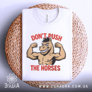 Футболка з конем білого кольору, зображена зверху на плетеній основі, фон світло-сірий, принт з конем, що показує м'язи, з написом 'DON'T PUSH THE HORSES' червоного кольору.