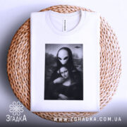 Футболка з Моною Лізою, білого кольору, складена на плетеній кошику, фон світло-сірий, принт зображає Мону Лізу з інопланетянином, деталі принта чіткі, з елементами чорного і сірого.