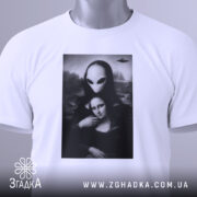 Футболка з Моною Лізою, білого кольору, складена на поверхні, фон світло-сірий, принт зображає Мону Лізу з інопланетянином, на футболці є етикетка з зеленим шнурком.