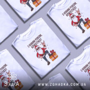 Футболка з Новим Роком, біла, зображена на манекені, фон світло-сірий, принт з дідом Морозом у червоному костюмі, який піднімає руку в жесті "рок", поряд з подарунком.