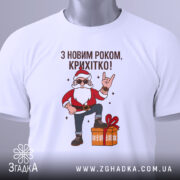Футболка з Новим Роком, біла, складена на столі, фон світло-сірий, принт з дідом Морозом у червоному костюмі, який піднімає руку в жесті "рок", з зеленим ярликом.
