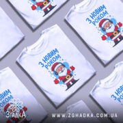 Футболка з Новим Роком, білого кольору, зображена з фронтального ракурсу на манекені, фон світло-сірий, принт з веселим Сантою в навушниках, з написом 'З НОВИМ РОКОМ' у верхній частині.
