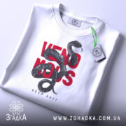 Футболка з отруйною змією, білого кольору, зображена в складеному вигляді на світлому фоні, принт з чорної змії на червоному тексті 'VENOMOUS KEEP AWAY', з зеленим ярликом.