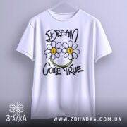 Футболка з ромашками, білого кольору, підвішена на вішалці, фон світло-сірий, принт з двома ромашками та написом 'DREAM COME TRUE' у чорному та зеленому кольорах.