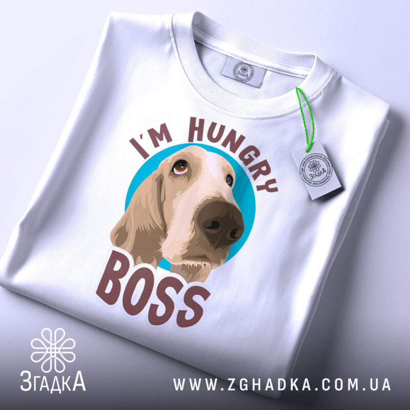 Футболка з собакою, білого кольору, складена на поверхні, фон світло-сірий, принт з собакою та написом 'I'M HUNGRY BOSS' розташований по центру, з зеленим ярликом.