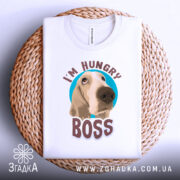 Футболка з собакою, білого кольору, складена на плетеній кошику, фон світло-сірий, принт з собакою та написом 'I'M HUNGRY BOSS' розташований по центру.