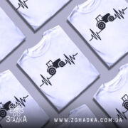 Футболка з трактором білого кольору, зображена з близького ракурсу, на фоні світло-сірого градієнта, принт з трактором та лінією, що нагадує кардіограму, виконаний в чорному кольорі.