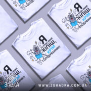 Футболка за будь-який кіпіш, біла, зображена зверху на світло-сірому фоні, кілька футболок в одному кадрі, принт з котом у синіх штанах, текст чорний і блакитний.