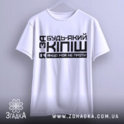 Футболка за кіпіш: біла футболка, підвішена на вішалці, з чорним принтом, що містить текст "Будь-який з Кіпіш, якщо моя не проти", фон світло-сірий, ракурс спереду.