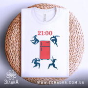 Футболка забіг до холодильника. Біла футболка, складена на кошику, з принтом червоного холодильника та фігурами людей, що стрибають. Ракурс зверху, фон світлий, футболка розташована на плетеній основі. Час на футболці вказано як 21:00.