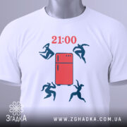 Футболка забіг до холодильника. Біла футболка, складена на поверхні, з принтом червоного холодильника та фігурами людей, що стрибають. Ракурс зверху, фон світлий, на футболці є етикетка з зеленим шнурком.