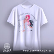 Футболка забула вийти заміж. Біла футболка з коротким рукавом, підвішена на вішалці. Принт дівчини з рожевим волоссям займає центральне місце. Фон світло-сірий, що робить акцент на дизайні футболки.