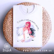 Футболка забула вийти заміж. Біла футболка, складена на плетеному кошику. Принт з дівчиною з рожевим волоссям чітко видимий. Фон натуральний, що надає елегантності зображенню.