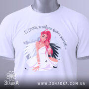 Футболка забула вийти заміж. Біла футболка, складена на столі, з видимим принтом дівчини з рожевим волоссям. На футболці видно етикетку з зеленим шнурком. Фон світлий, що підкреслює яскравість принта.