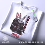 Футболка заяча мафія, біла, зображена зверху, складена, фон світлий, принт з зображенням кролика в чорному костюмі з мечем, текст на принті японською мовою та написом 'ZAYKUZA', на футболці зелений ярлик.