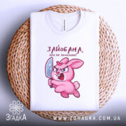 Футболка зайобана але не зломлена, біла, складена на плетеній основі, фон світло-сірий, принт з рожевим зайцем, що тримає ніж, з виразом гніву.