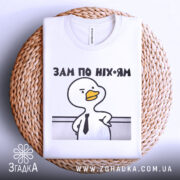 Футболка зам по ніхуям, біла, складена на плетеній кошику, фон світло-сірий, принт з качкою в краватці та написом 'ЗАМ ПО НІХ-ЯМ'.