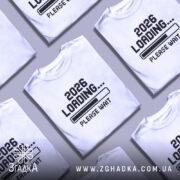 Футболка завантаження року, біла футболка на манекені, з принтом '2026 LOADING... PLEASE WAIT' у чорному кольорі, фон світло-сірий, деталі принта чіткі та контрастні.