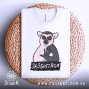 Футболка зазбогійся, білого кольору, зображена зверху на плетеній основі, принт з ведмедем з червоними очима та написом 'ЗАБОТИСЯ', видно етикетку на горловині.