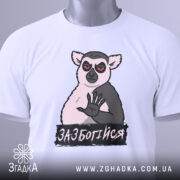 Футболка зазбогійся, білого кольору, зображена зверху, на ній видно принт з ведмедем, що має червоні очі, та напис 'ЗАБОТИСЯ', на футболці також є етикетка з зеленим шнурком.