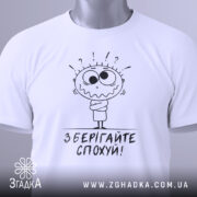 Футболка зберігайте спохуй. Біла футболка, складена на столі, з видимим ярликом, фон світлий, принт з мультяшним персонажем, що виглядає здивованим, з написом 'Зберігайте спохуй!' під ним.