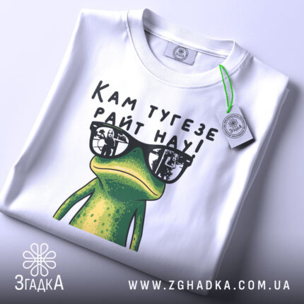 Футболка жаба кам тугезе, біла, складена на поверхні, фон світлий, принт з жабою в окулярах, текст "Кам тугезе райт нау!" над жабою, на футболці є етикетка.