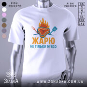 Футболка жарю м`ясо, біла, зображена з фронтального ракурсу, фон світло-сірий, принт з зображенням шматка м'яса з вогнем і кухонними приладами, текст "ЖАРЮ НЕ ТІЛЬКИ М'ЯСО" яскравими кольорами.