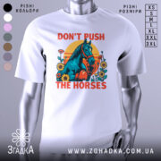 Футболка жарт і стиль. Біла футболка з яскравим принтом, на якому зображений кінь у рукавичках, оточений квітами на фоні жовто-оранжевого сонця. Футболка представлена на манекені з металевим блиском, фон нейтральний сірий.