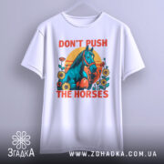 Футболка жарт і стиль. Біла футболка з яскравим принтом, на якому зображений кінь у рукавичках, оточений квітами на фоні сонця. Футболка підвішена на вішалці, фон нейтральний сірий.